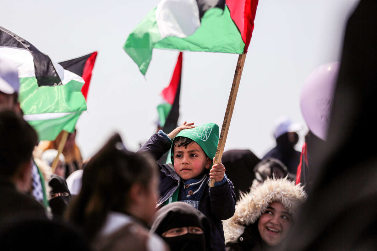A little boy holds a Palestinian flag while on someone's shoulders at a rally