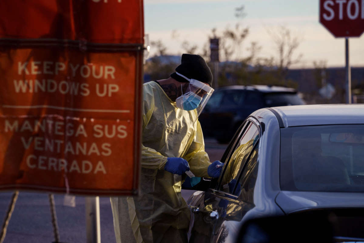 A health care worker administers a covid-19 test to a patient through a car window