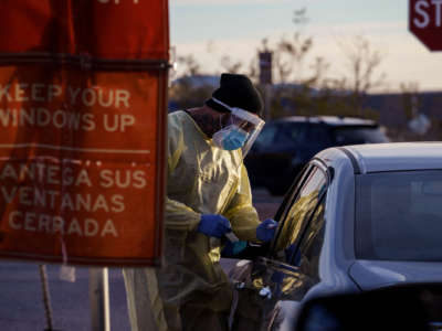 A health care worker administers a covid-19 test to a patient through a car window