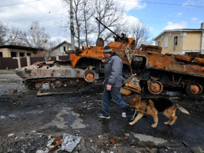 A man walks by with his dog past destroyed military equipment of the Russian army against the background of severe destruction in Bucha, Ukraine, on April 4, 2022.