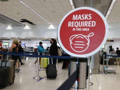 A sign reading, 'masks required in this area,' is seen as travelers prepare to check-in for their flight at the Miami International Airport on February 1, 2021 in Miami, Florida.