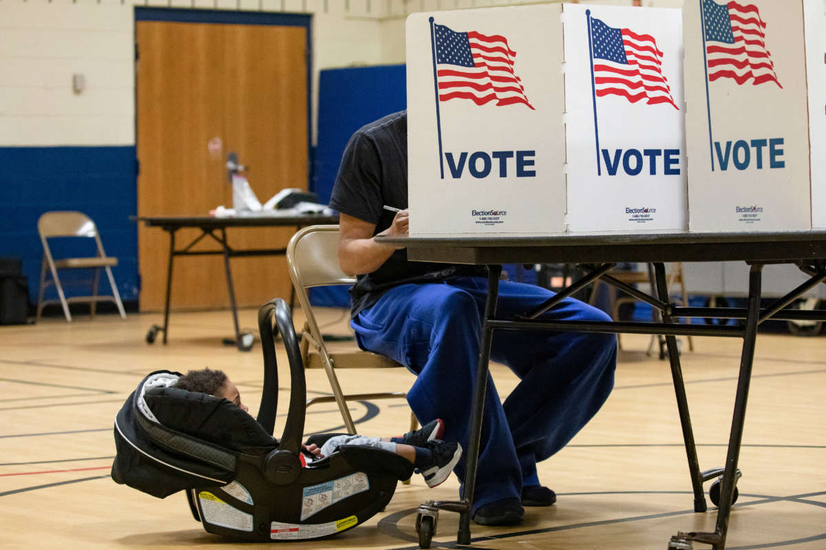 A boy in a child carrier looks at his father as he casts his ballot for the Democratic presidential primary election at a polling place in Armstrong Elementary School on March 3, 2020, in Herndon, Virginia.