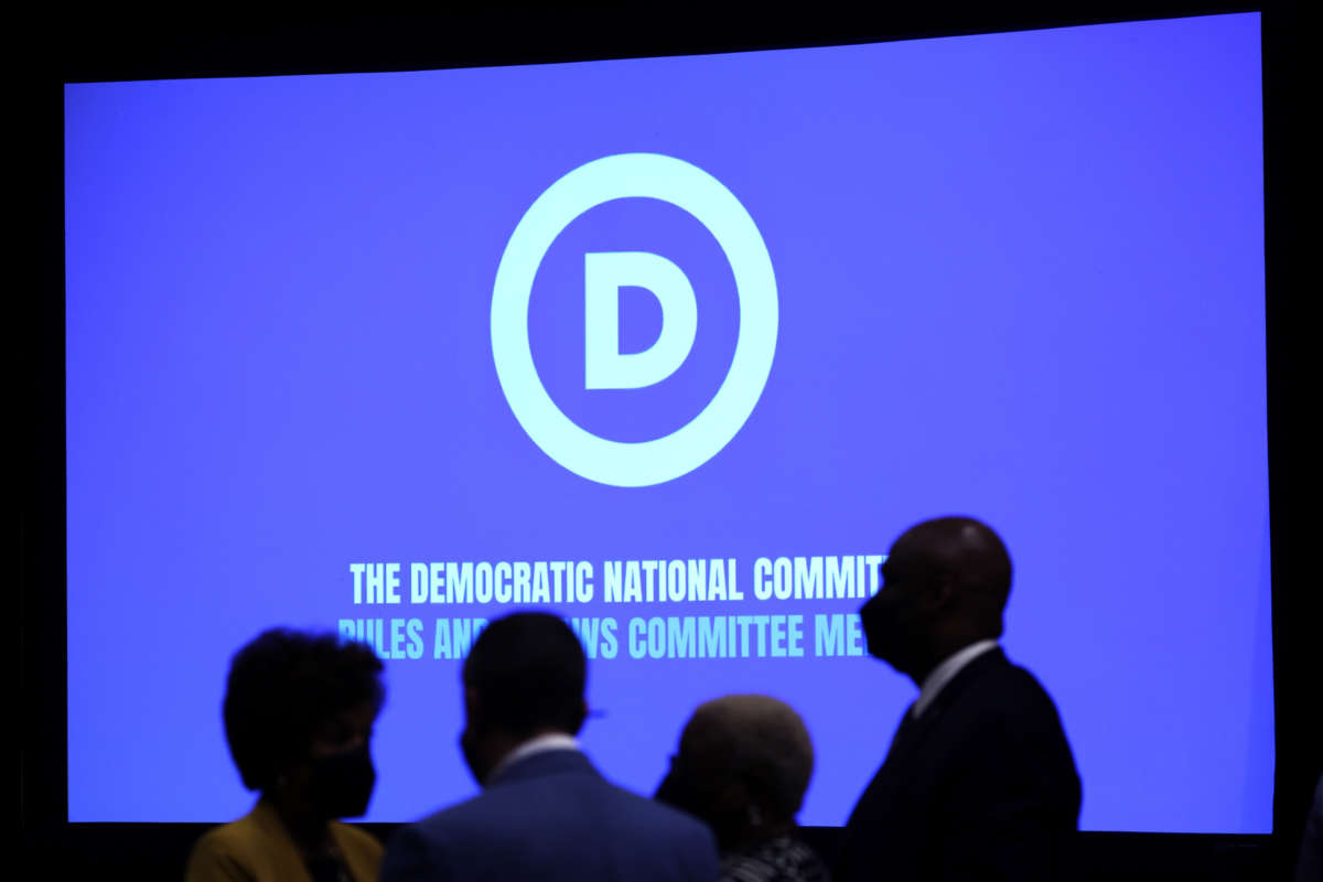 People walk in front of a projection screen showing the DNC logo