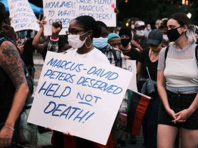 Protesters holding a sign that reads "Marcus-David Peters Deserved HELP Not DEATH!!" at a demonstration on July 28, 2020, in Richmond, Virginia. Marcus-David was a 24-year-old Black man who was shot and killed by a Richmond police officer on May 14, 2018, while experiencing a mental health crisis.