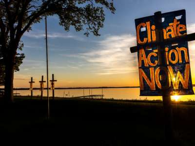 A sign placed near a body of water reads "CLIMATE ACTION NOW"