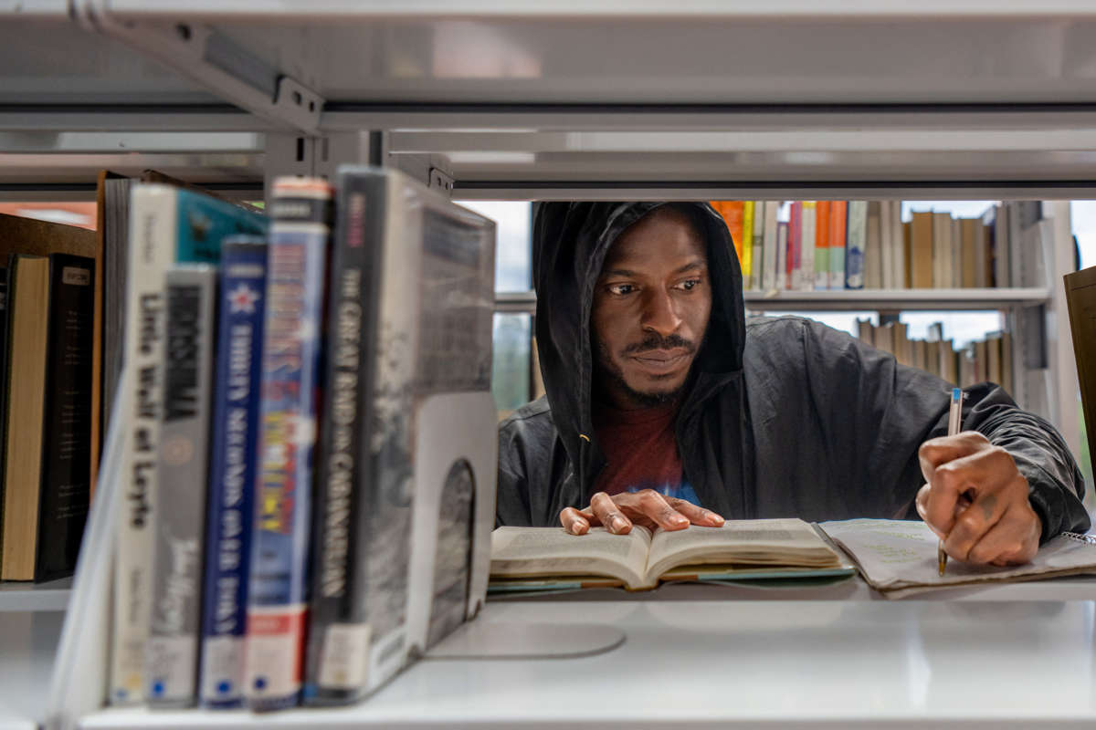 A man takes notes from an open book on a library bookshelf