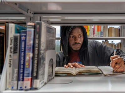 A man takes notes from an open book on a library bookshelf