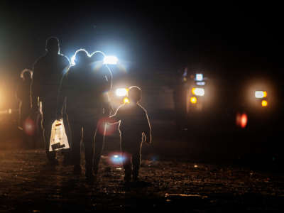 Immigrants are silhouetted in the headlights of ice vehicles