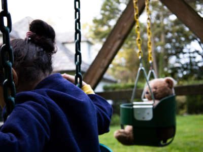 Child on swing set with teddy bear