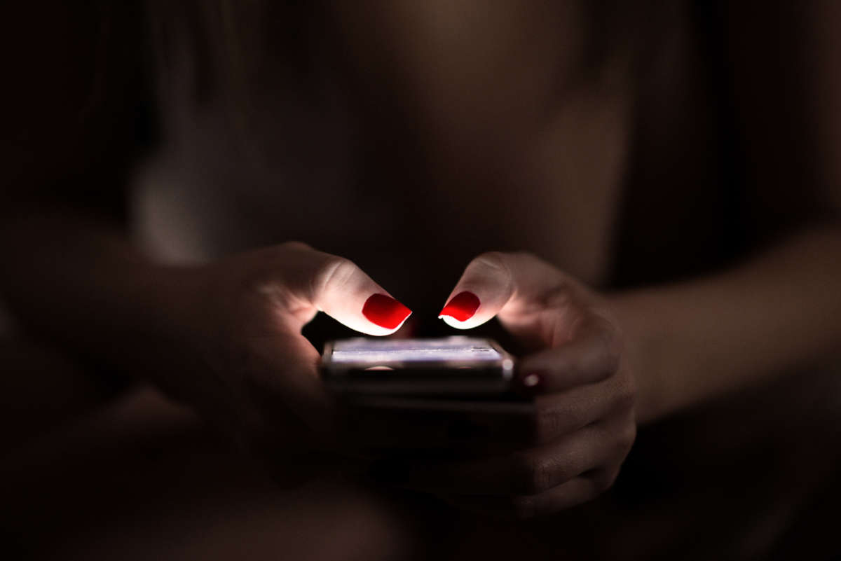 Person with red fingernail polish uses cell phone in the dark