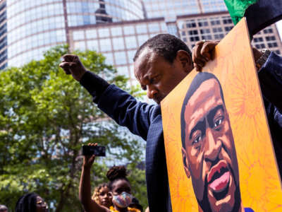 A man raises a fist while holding a portrait of the late George Floyd while at an outdoor protest