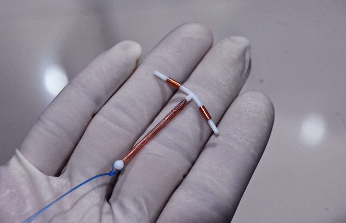 A medical professional holds a copper IUD in their gloved hand