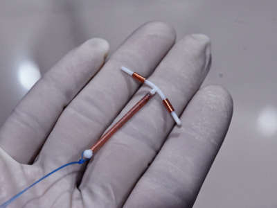 A medical professional holds a copper IUD in their gloved hand