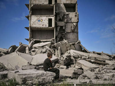 A boy sits among the rubble of what was once a building