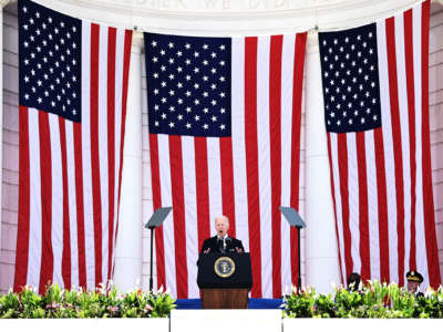 Joe Biden shouts into a microphone while positioned in front of three u.s. flags