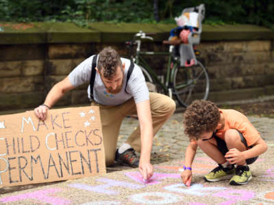 A father and child use chalk to write messages in support of the expanded child tax credit