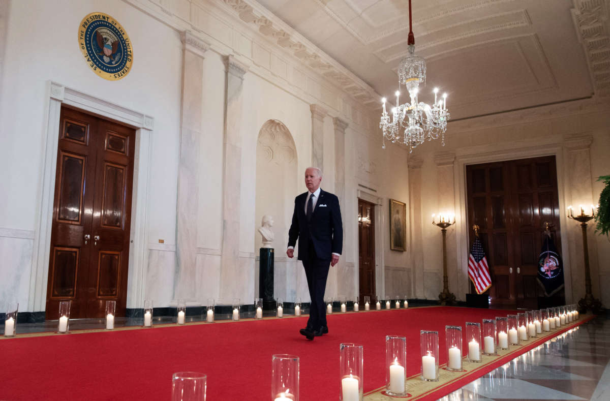 Joseph Robinette Biden walks down a long hallway lined with candles