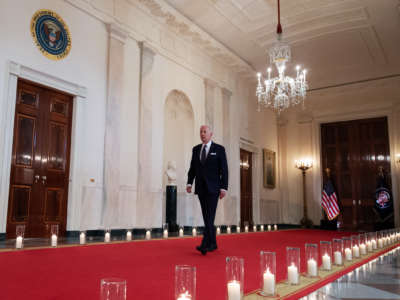Joseph Robinette Biden walks down a long hallway lined with candles