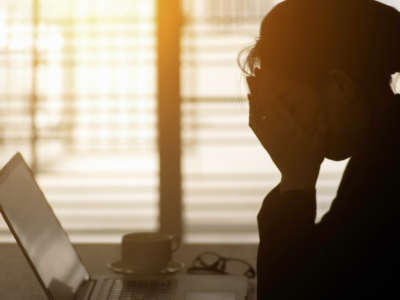 Person with head in hands at computer, backlit by sun through window