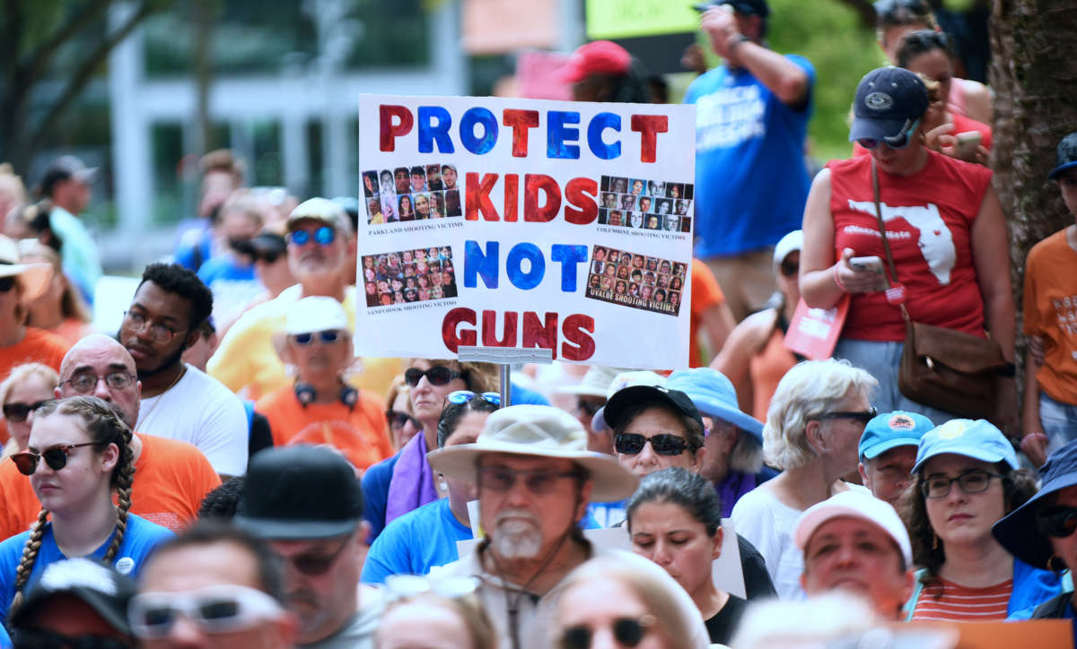 A person holds a sign reading "PROTECT KIDS, NOT GUNS" during an outdoor protest
