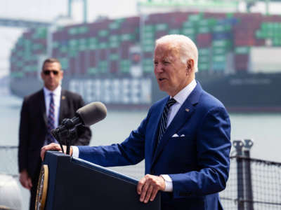 Joseph Robinette Biden speaks into a microphone at a podium near commercial docks