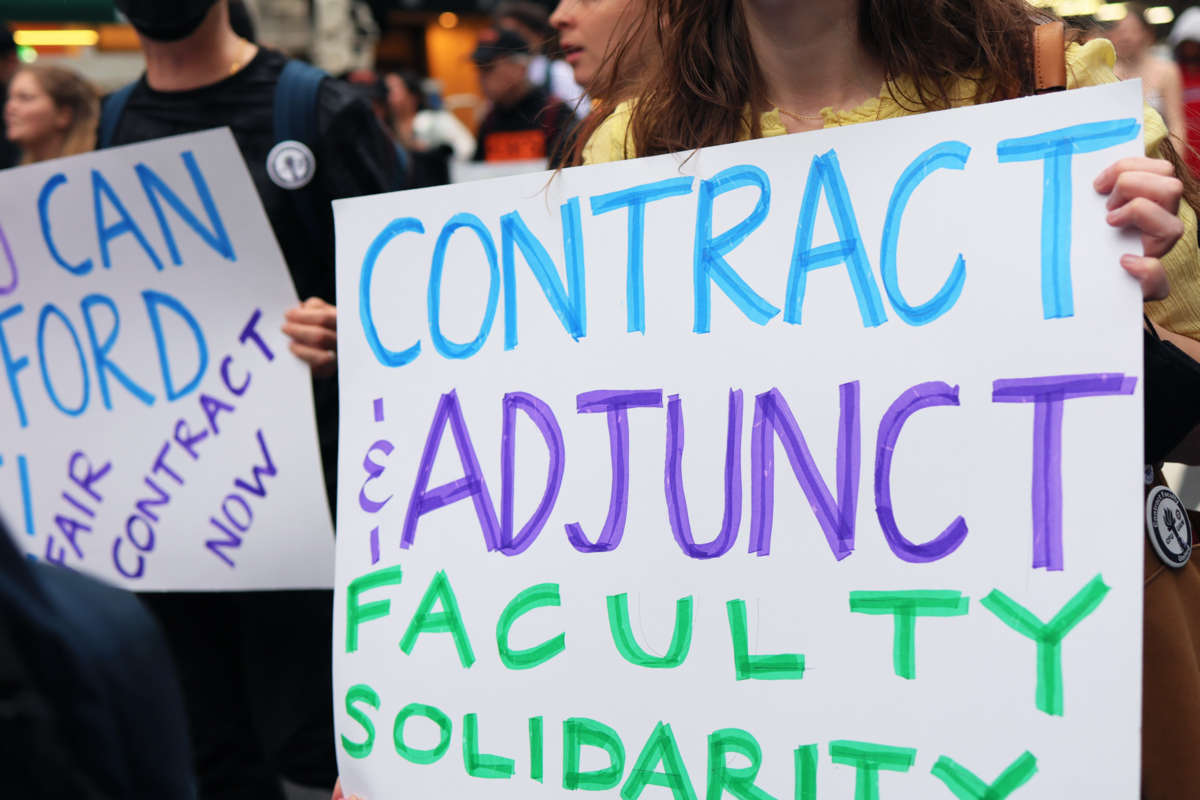 A protester holds a sign reading "Contract and adjunct faculty solidarity" during an outdoor protest