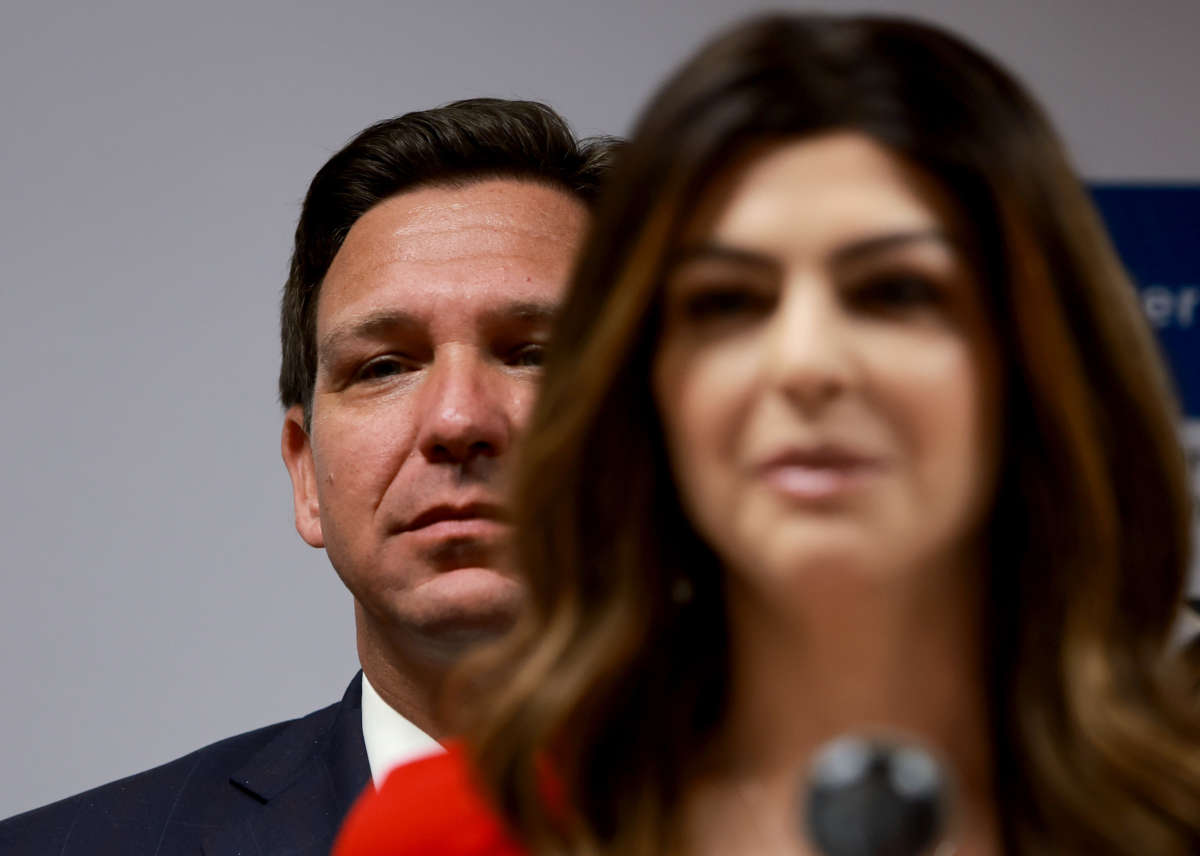 Gov. Ron Desantis lurks behind his wife as she speaks at a podium
