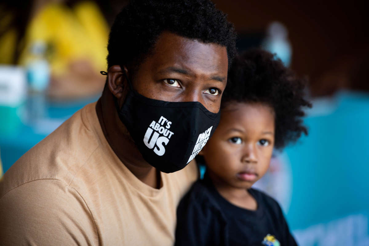 Jelani Hendrix and his three-year-old son L.J. staff the Black Alliance For Just Immigration (BAJI) booth at a Juneteenth celebration at Magic Johnson Park in Willowbrook, California, on June 17, 2022.