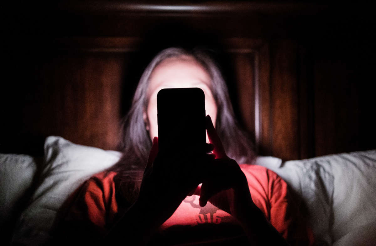 Woman laying in bed and checking updates on smartphone.