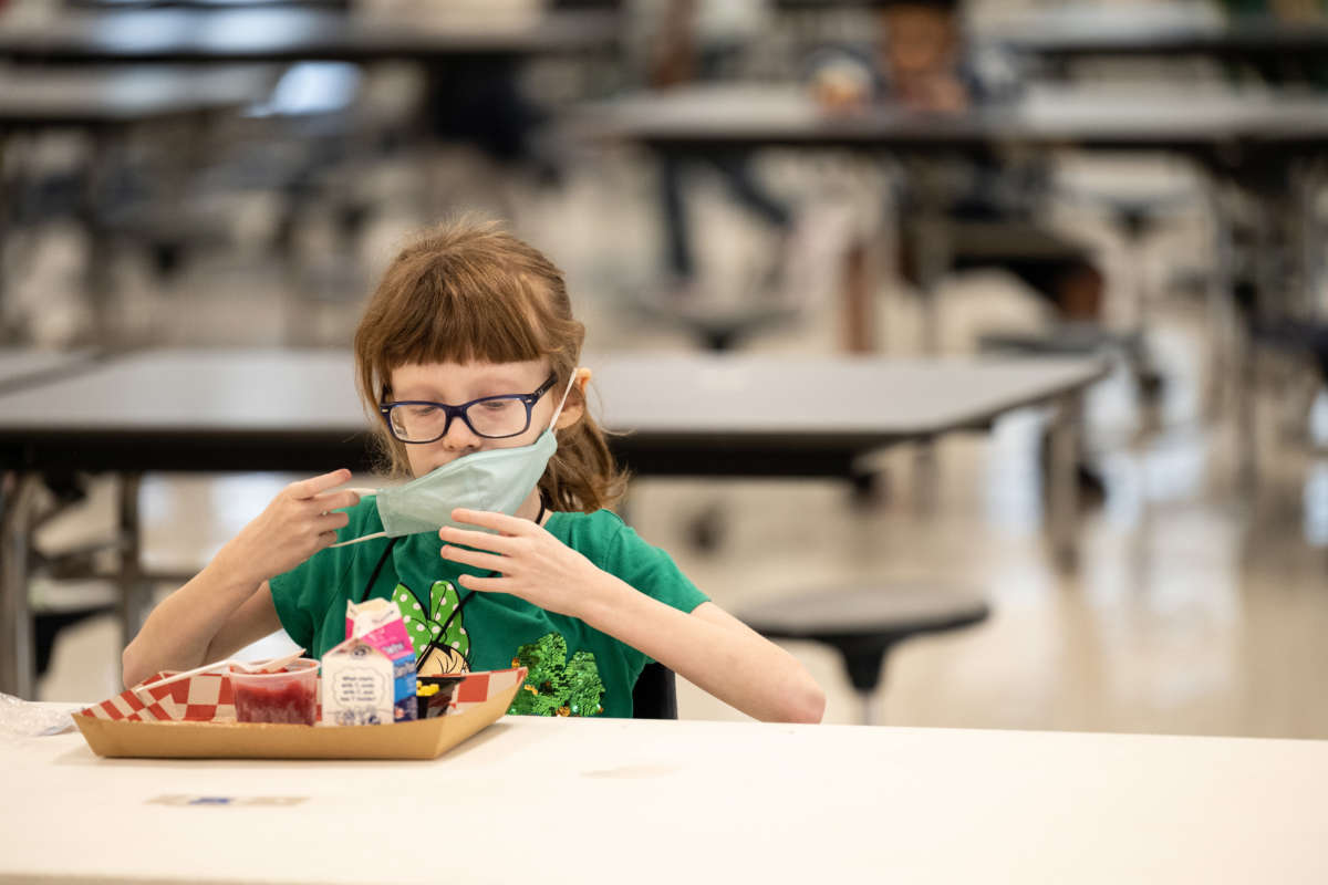 A child puts her mask back on after finishing lunch at a socially distanced table in the cafeteria of Medora Elementary School on March 17, 2021, in Louisville, Kentucky.