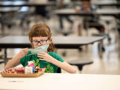 A child puts her mask back on after finishing lunch at a socially distanced table in the cafeteria of Medora Elementary School on March 17, 2021, in Louisville, Kentucky.