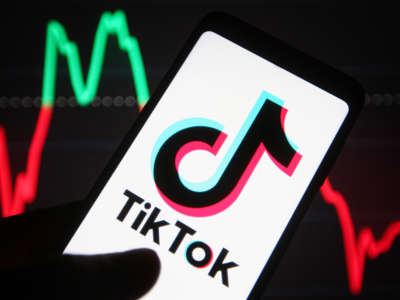 TikTok logo is seen on a smartphone in a hand, in front of line graph