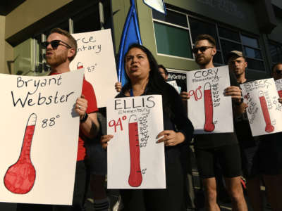 People hold up signs as they take part in a protest outside of the Denver Public Schools administration building to demand equity for students attending classes in excessively hot classrooms on August 26, 2019, in Denver, Colorado.