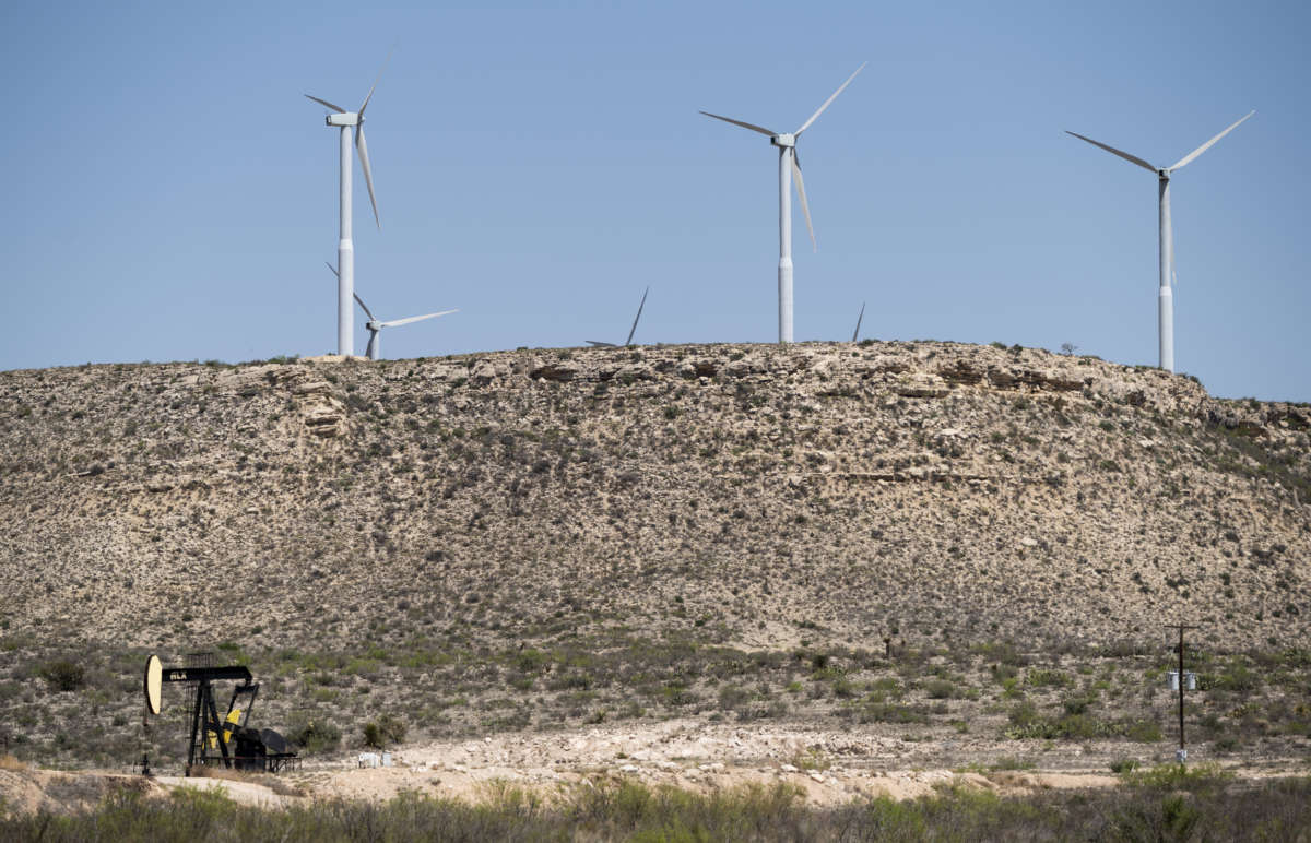 A pumpjack pumps oil below wind turbines near Fort Stockton, Texas, on Saturday, April 10, 2021.
