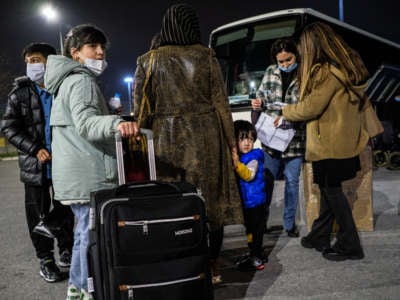 Afghani refugees with suitcases wait to board buses in Greece