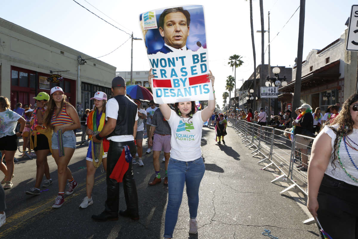 A person holds a poster with a picture of Ron DeSantis that says "Won't be erased by desantis" during a Florida Pride event