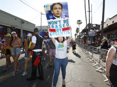 A person holds a poster with a picture of Ron DeSantis that says "Won't be erased by desantis" during a Florida Pride event
