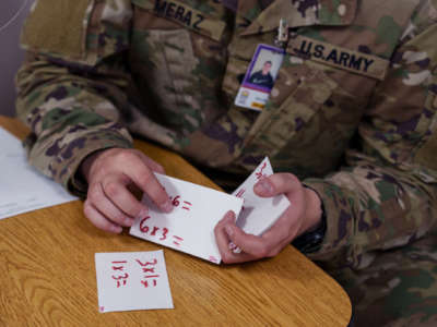 A man in army camoflague goes over math flash cards in the class he's teaching