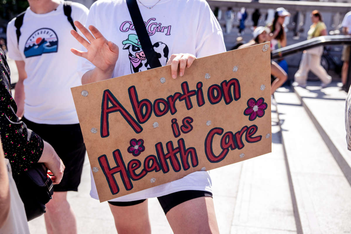 a person holds a sign reading "ABORTION IS HEALTHCARE" at an outdoor protest