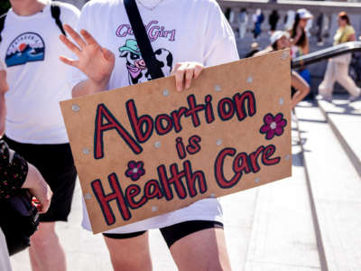 a person holds a sign reading "ABORTION IS HEALTHCARE" at an outdoor protest