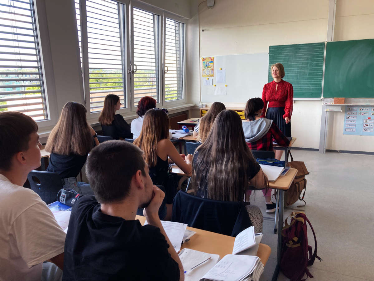 A woman standing in front of a chalkboard teaches a class of students