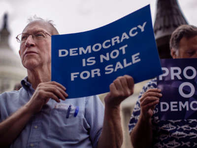 A man holds a sign reading "DEMOCRACY IS NOT FOR SALE" during a protest