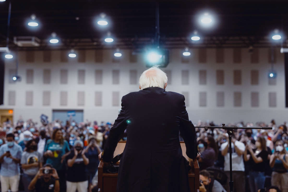 Sen. Bernie Sanders is seen from behind, standing at a podium before a packed audience