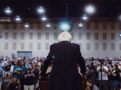 Sen. Bernie Sanders is seen from behind, standing at a podium before a packed audience