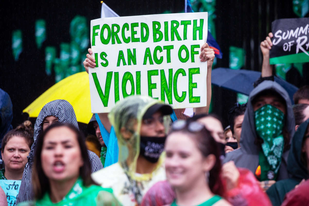 A person holds a sign reading "FORCED BIRTH IS AN ACT OF VIOLENCE" during an outdoor protest