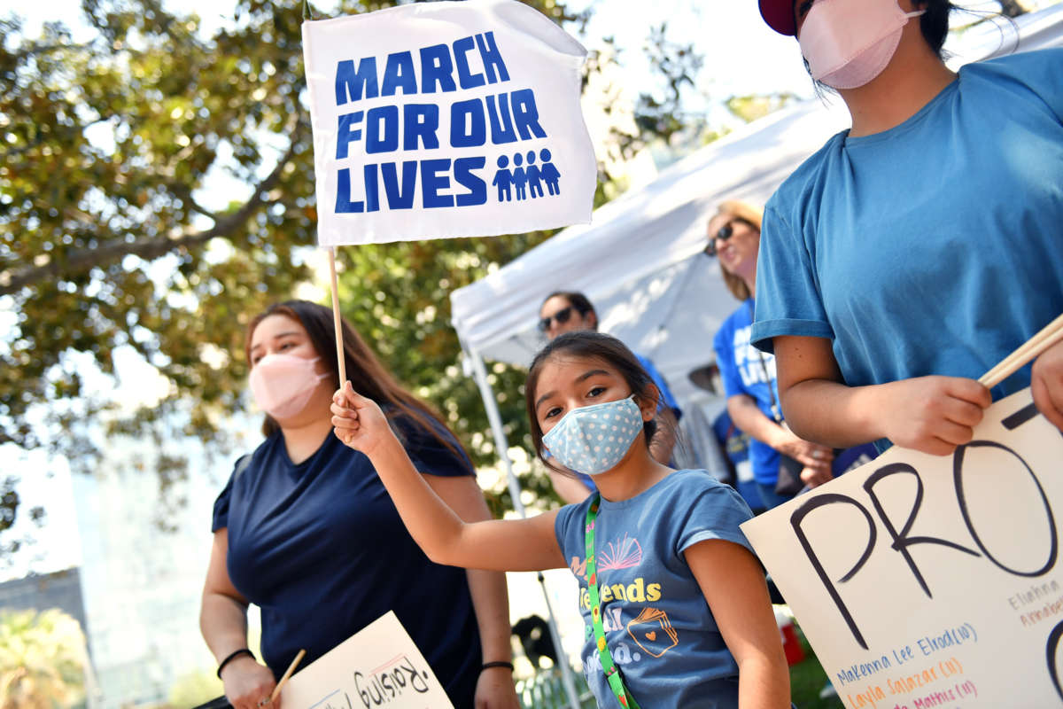 A masked school child waves a flag reading "MARCH FOR OUR LIVES" during an outdoor protest