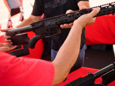 A clerk hands a customer a featureless AR-15 style rifle from TPM Arms LLC on display for sale at the company's booth at the Crossroads of the West Gun Show at the Orange County Fairgrounds on June 5, 2021, in Costa Mesa, California.