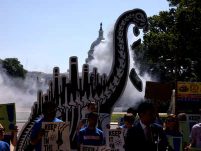 Activists simulate smoke coming from the back of a cardboard cut out of a dinosaur during an 'End Fossil Fuel' rally near the U.S. Capitol on June 29, 2021, in Washington, D.C.