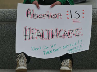 A protester hold a sign that reads, "Abortion IS HEALTHCARE. Don't Like it? THEN DON'T GET ONE!!! SIMPLE!!!"