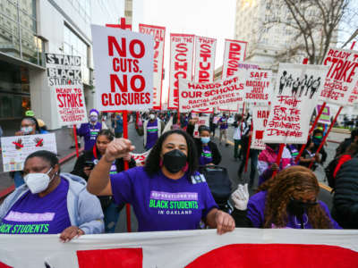 Parents in Oakland protest with signs that say "No cuts no closures"